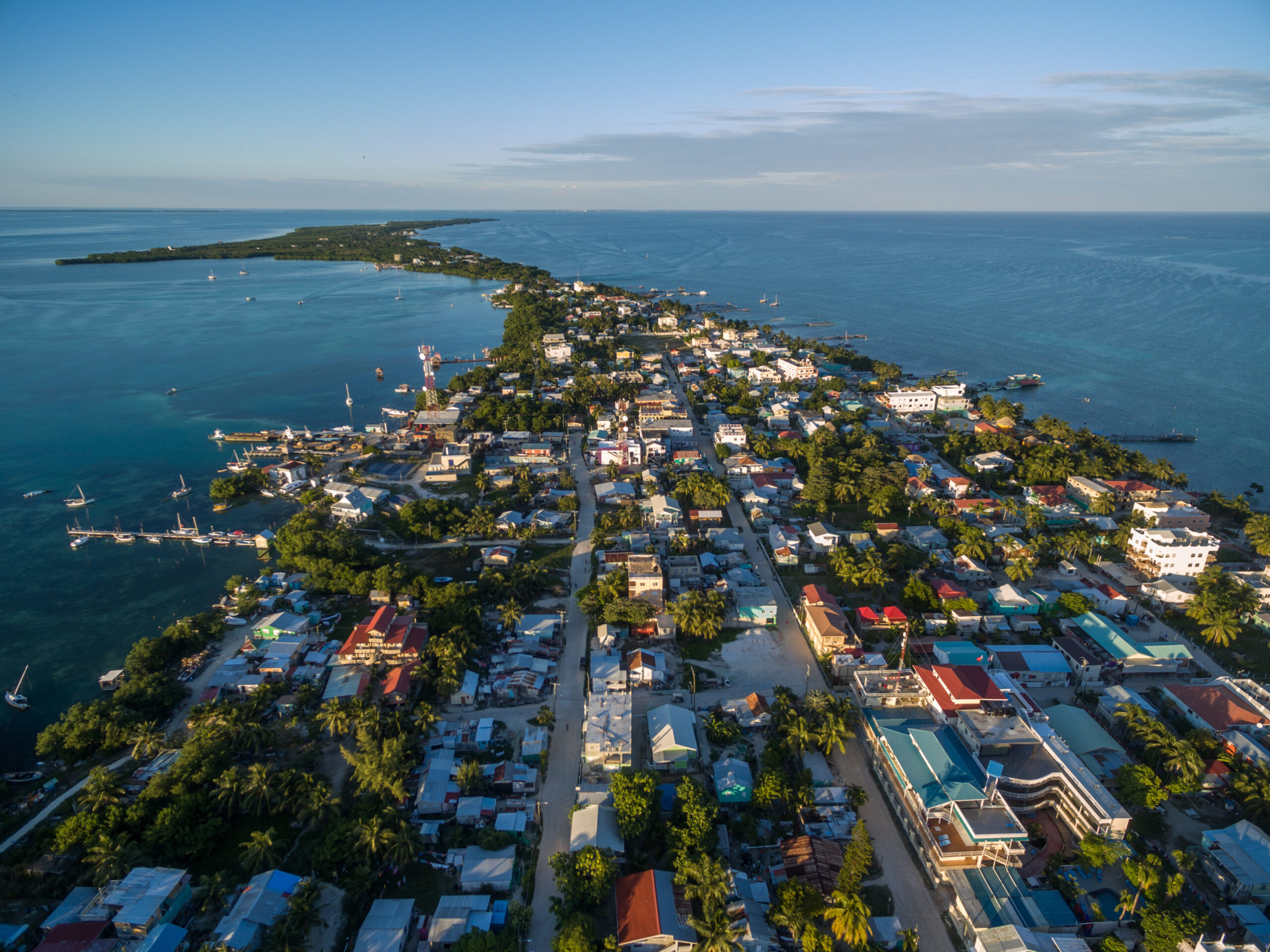 Caye Caulker Island in Belize, Caribbean Sea. Drone Point of View. Small island surrounded by the ocean on a cloudy day. Rooftops and streets can be seen on the tropical island below.