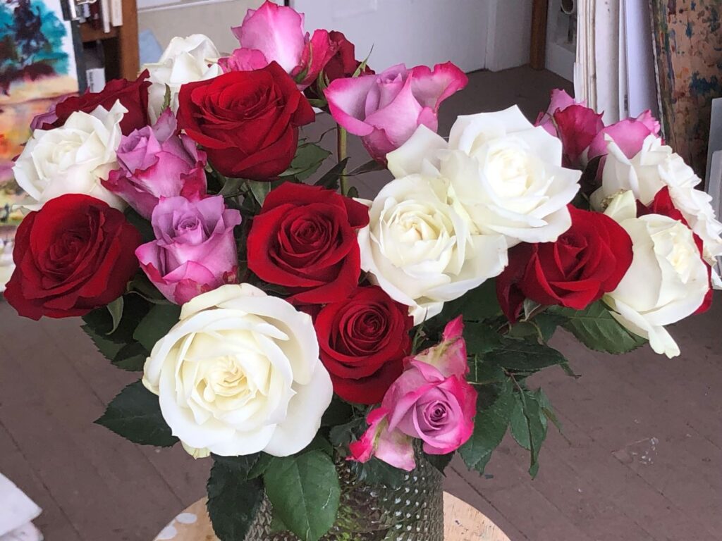 Photo of a bouquet of roses. They are white, red and pink in a green vase.