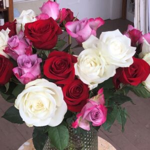Photo of a bouquet of roses. They are white, red and pink in a green vase.