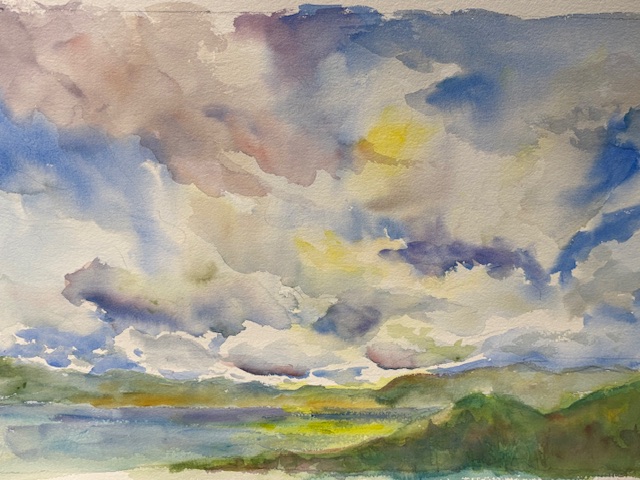 Expressive watercolor landscape titled 'Clouds Over Nagog.' The image is dominated by a dramatic sky filled with large, billowing clouds in shades of blue, white, purple, and yellow, suggesting an approaching storm or sunrise/sunset. Below the expansive sky is a landscape featuring a body of water (Nagog) flanked by rolling hills and patches of yellow and green fields.