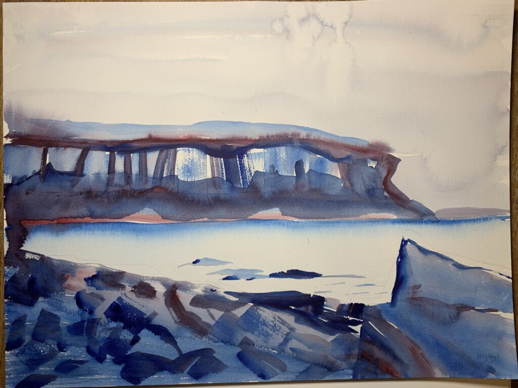 A tranquil watercolor scene of Lion's Head, depicting its limestone faces, obscured in many places by trees. The mid-ground shows the water. In the foreground is a beach of basketball sized rocks, leading to a large boulder that resembles a crooked sofa. Painted in Phthalo Blue and Alizarin Crimson, which mix to make a variety of purple shades.