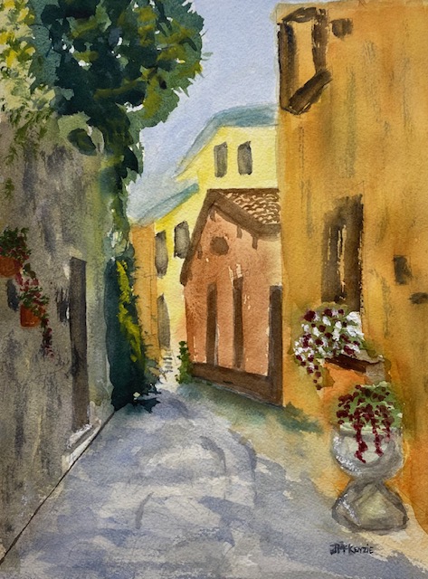Varenna Italy, original watercolor painting of a street with tan and yellow buildings on the right side of the street with a window box of white flowers. On the left side of the street is a darker greenish grey building covered over the top and side with foliage.